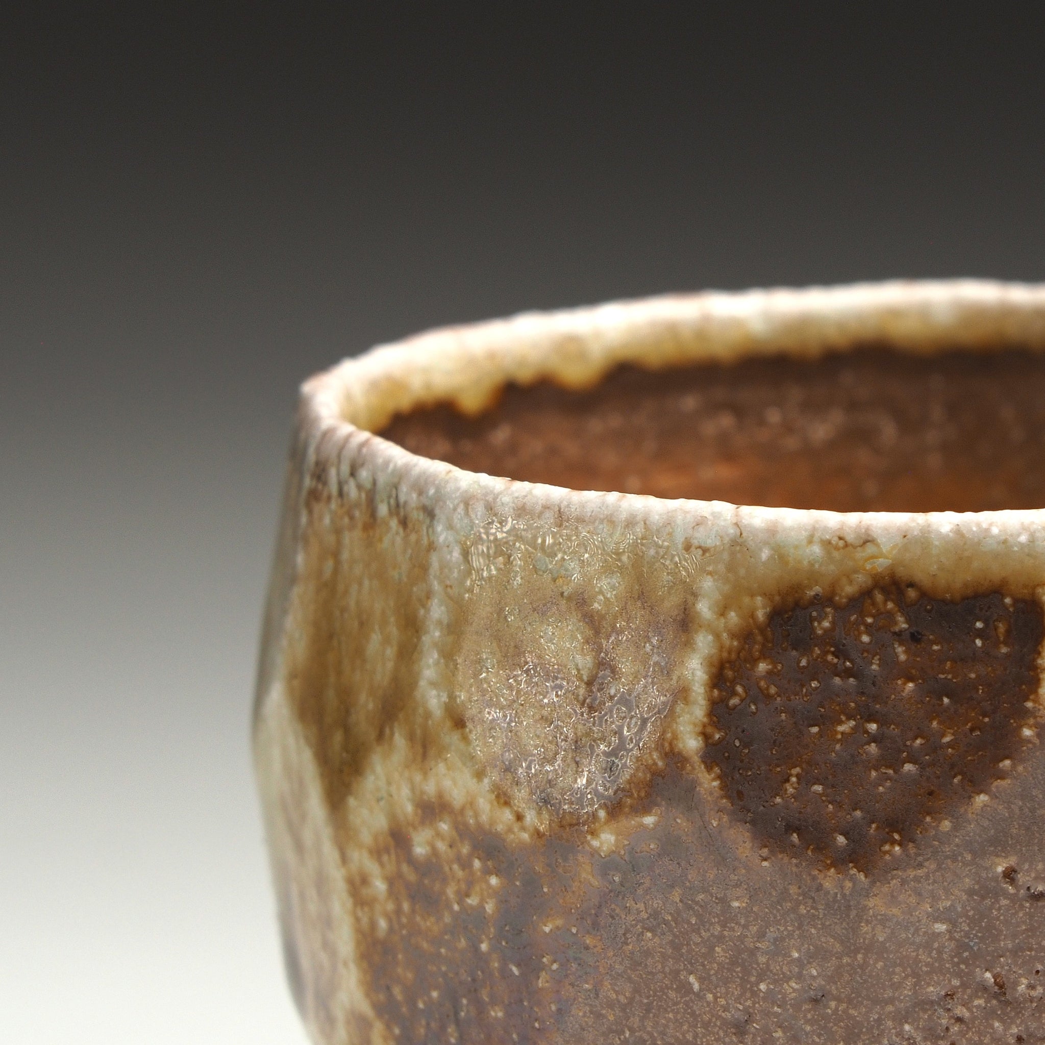Close-up of a Ryoen Shigaraki yunomi showing its brown clay surface and textured beige glaze around the rim.