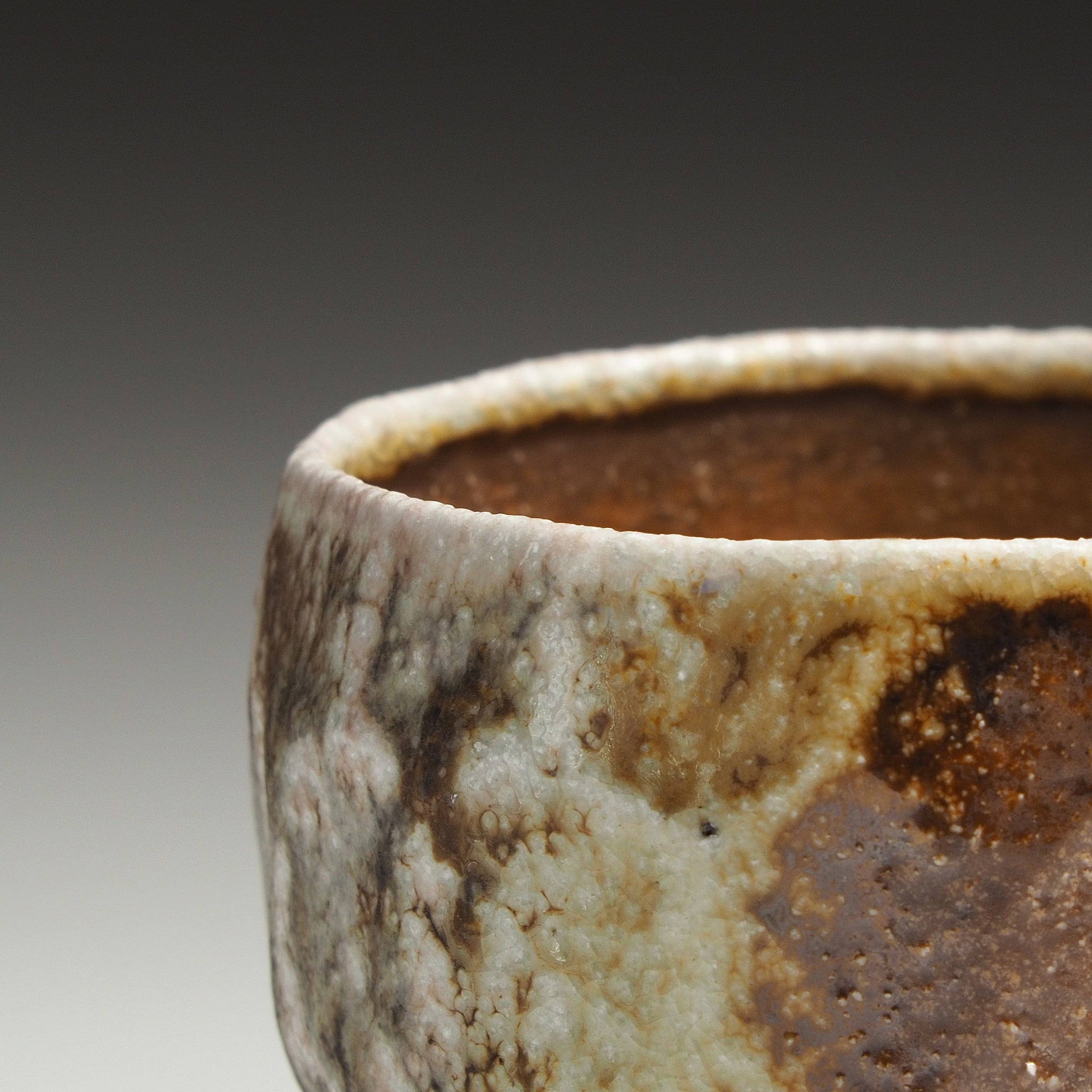 Close-up of a Ryoen handmade Shigaraki yunomi showing its irregular rim and mottled beige, brown, and gray glaze.