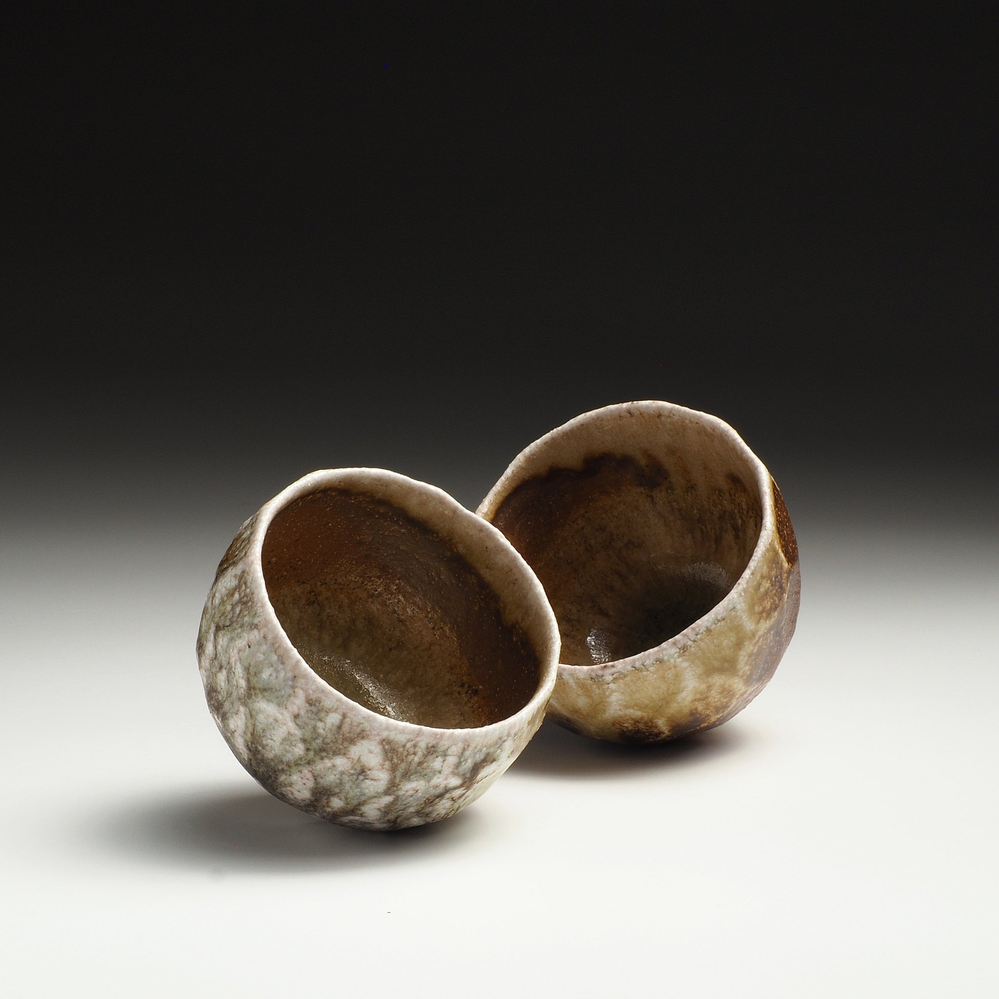 Two handmade Shigaraki teacups with a textured mottled glaze in earthy brown, beige, and gray tones.