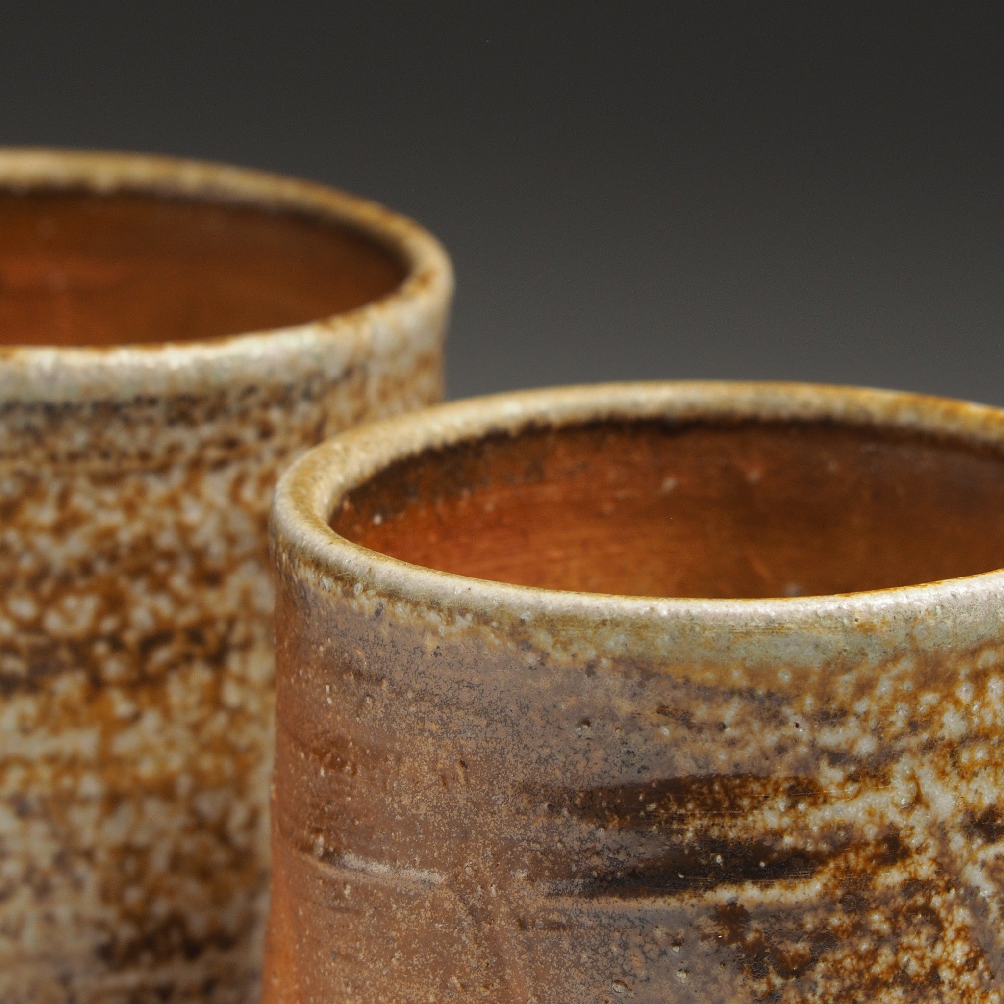 Close-up of two Yubae handmade Shigaraki yunomi teacups showing their warm brown interiors, rounded rims, and mottled beige ash-fired surfaces.