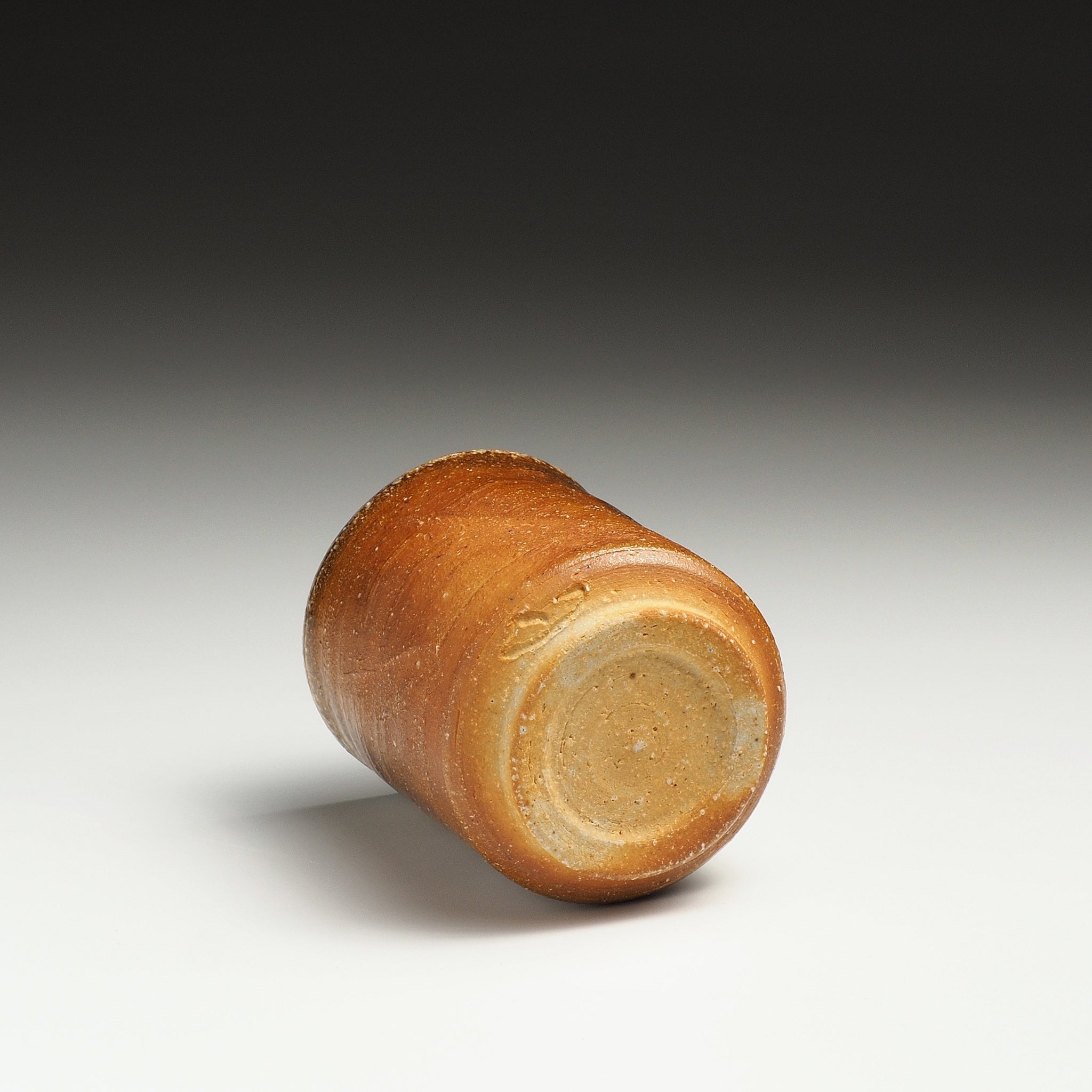 Yubae handmade Shigaraki yunomi resting on its side, showing the circular base and warm firing tones.
