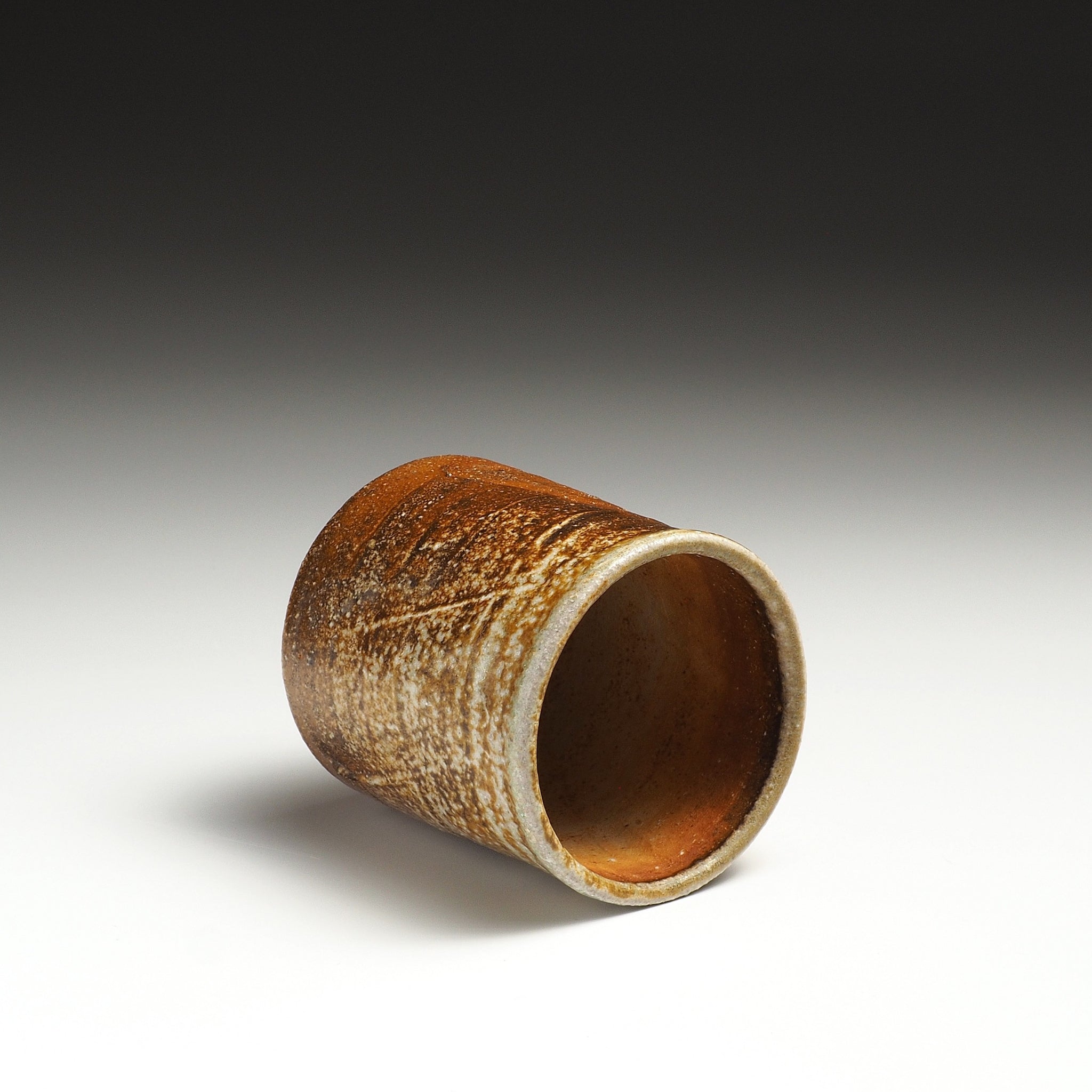 Yubae Shigaraki yunomi resting on its side, showing the dark interior and textured beige-brown surface.