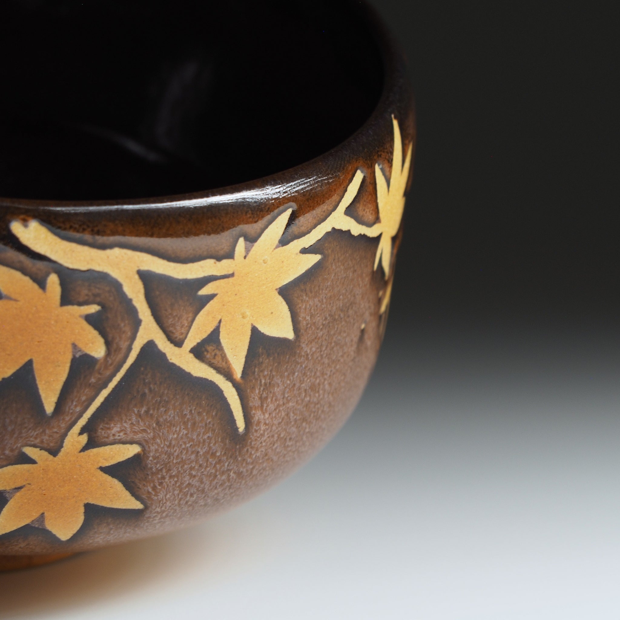 Yūkaede matcha bowl, full momiji branch pattern in negative-space clay against deep Nanasai Tenmoku glaze, Nunobiki Kiln