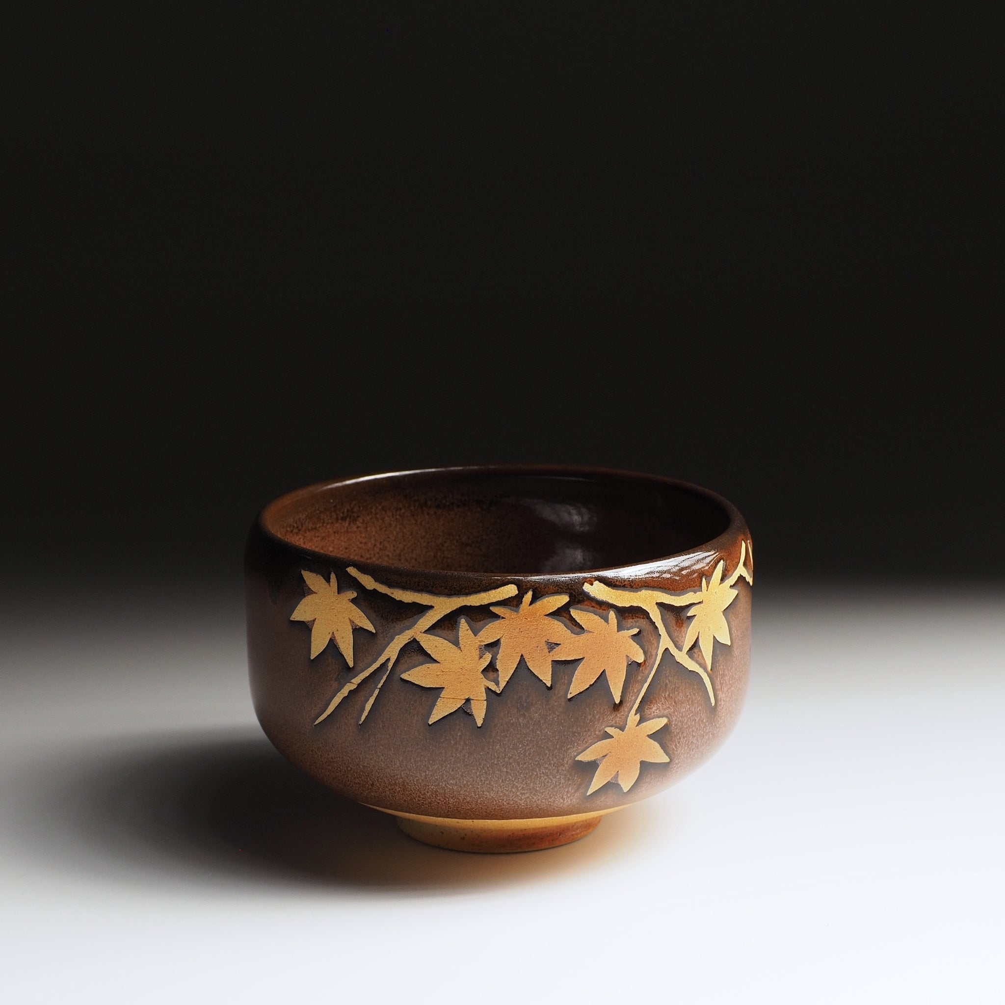 Yūkaede matcha bowl, natural light showing momiji branch descending across Nanasai Tenmoku glaze, Taro Kojima, Japan